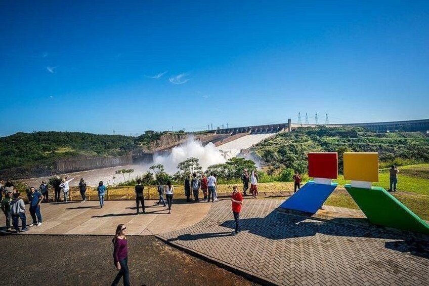 Una presa con agua que brota, una multitud de personas y estructuras geométricas coloridas. 1