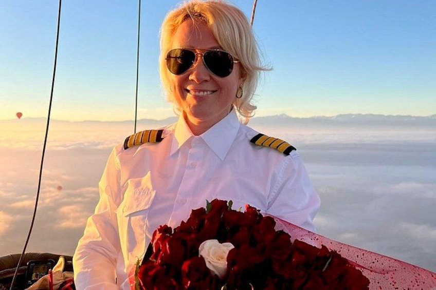 Una persona con uniforme blanco y hombreras, sosteniendo un ramo de rosas rojas, con un cielo despejado y nubes al fondo. 2