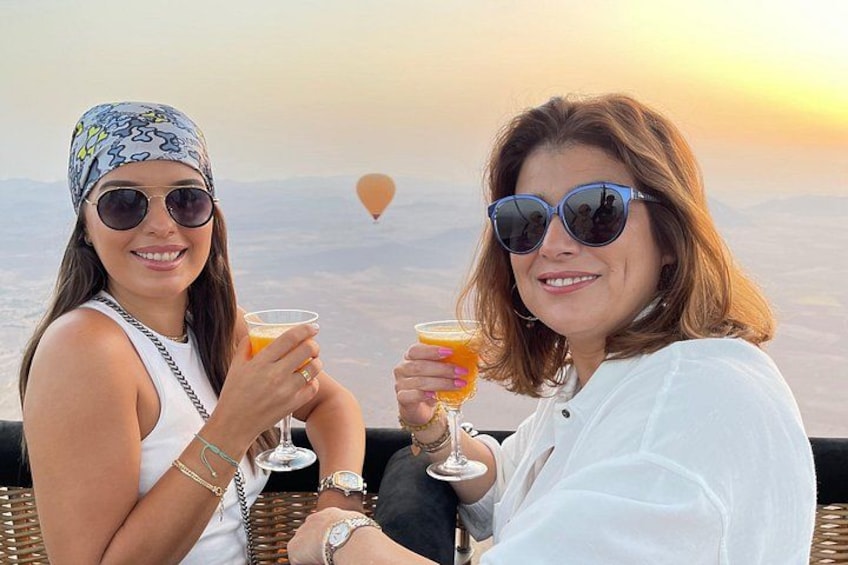 Dos personas sentadas al aire libre, sosteniendo bebidas, con una vista panorámica del paisaje de fondo. 1