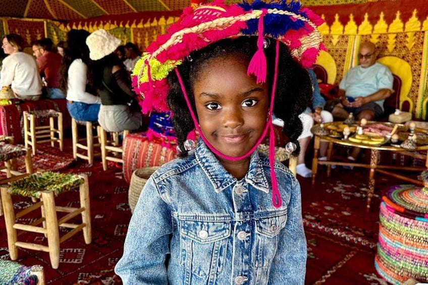 Una persona con chaqueta vaquera y sombrero colorido, con una alfombra estampada y muebles tradicionales al fondo. 5