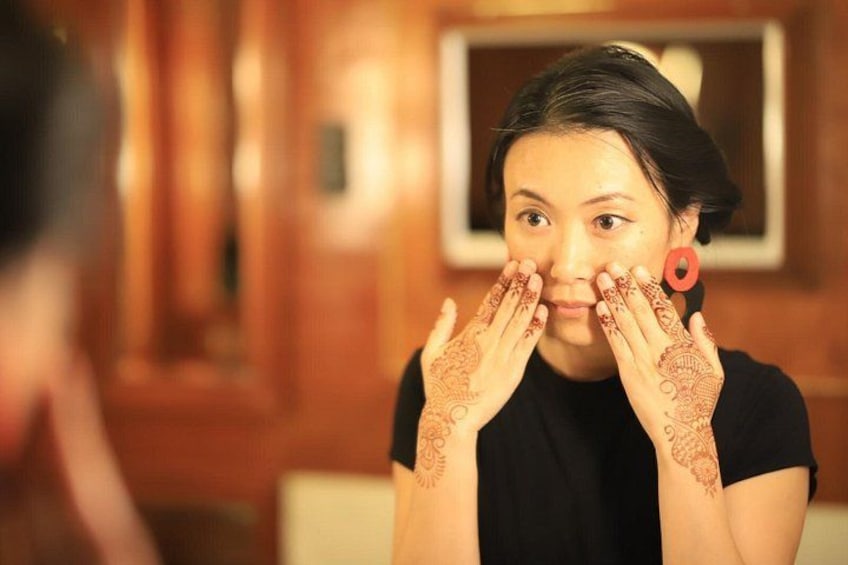 A person with henna designs on their hands and arms, wearing a black top, in a room with wooden walls and a mirror. 1