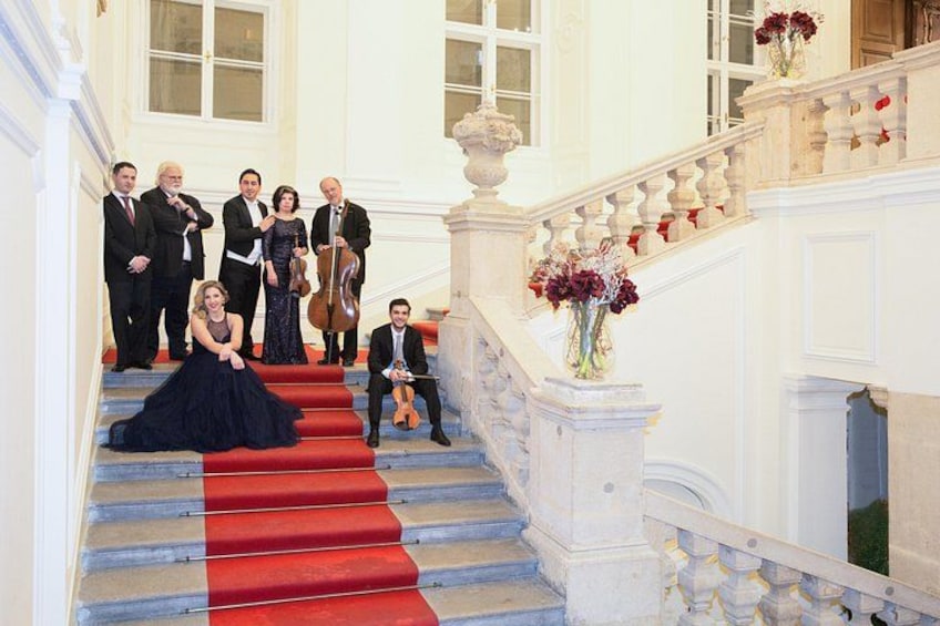 A group of people on a grand staircase with red carpet, white walls, and a balustrade. 3