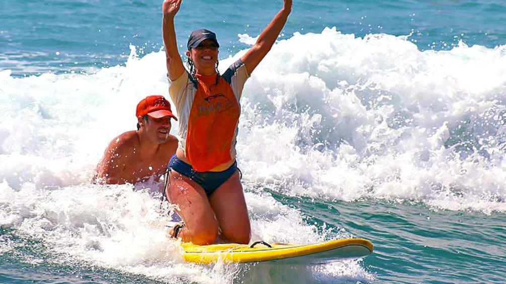 Two people surfing on a yellow surfboard in the ocean. 1