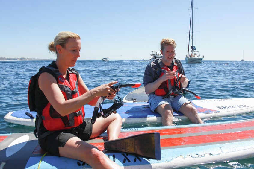 Two people on a kayak in the ocean with boats in the background. 3