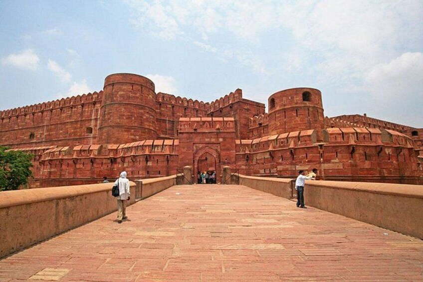 Een groot rood fort met een centrale poort, een verharde looppad en twee personen die foto's maken. 4