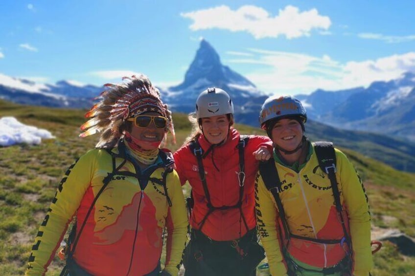 Three people wearing mountain biking gear on a grassy mountain slope with snow-capped peaks in the background. 3