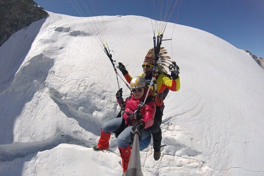 A person in a red jacket and helmet paragliding over a snow-covered mountain. 5
