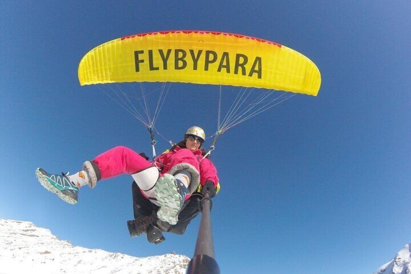 A person paragliding with a yellow canopy labeled "FLYBYPARA". 2