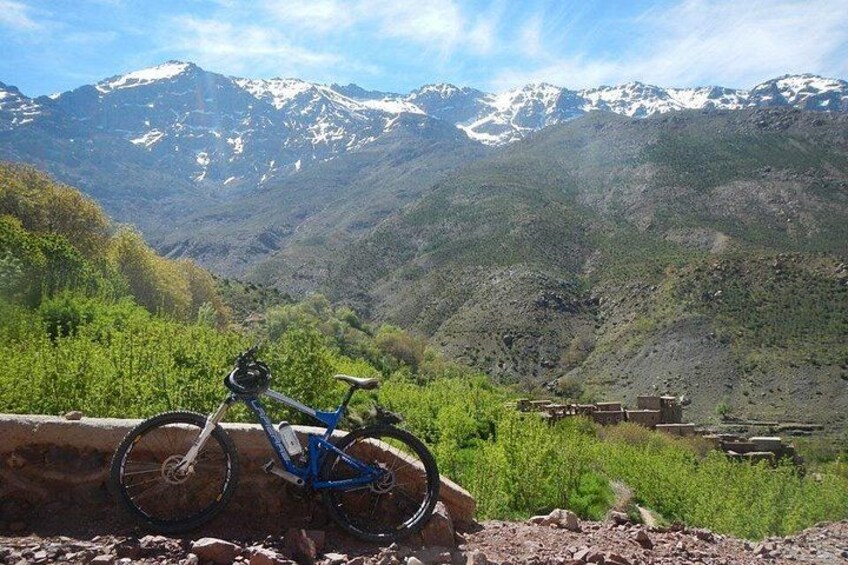 A mountain landscape with snow-capped peaks, a blue bicycle leaning against a wall, and traditional buildings in the valley. 1