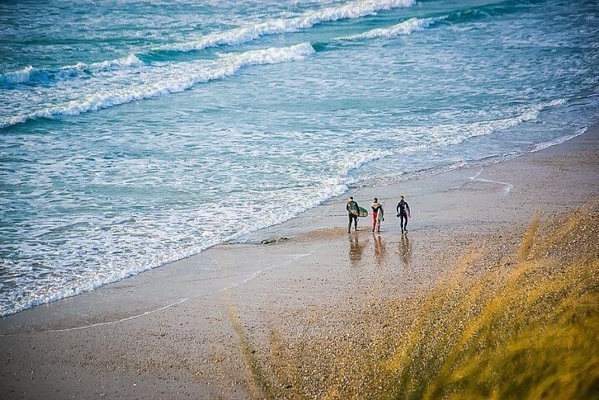 Three people walking along a beach with waves crashing onto the shore. 4