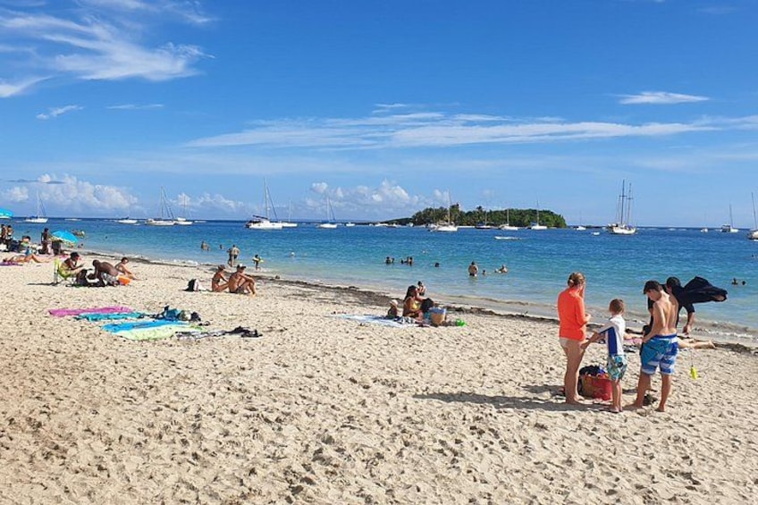 A beach with people sunbathing, a child playing, and boats in the water. 1