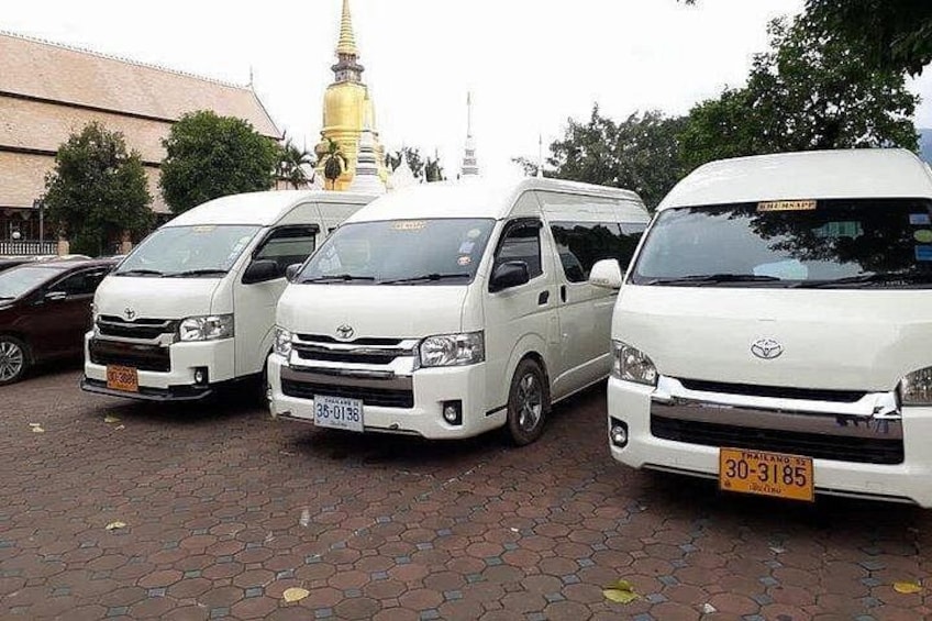 Tre vita Toyota-skåpbilar parkerade på en asfalterad yta, med en gyllene stupa i bakgrunden. 3