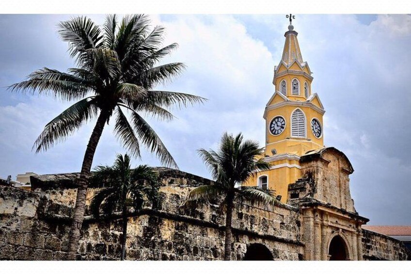 A historic church with a clock tower, palm trees, and an old stone wall. 4