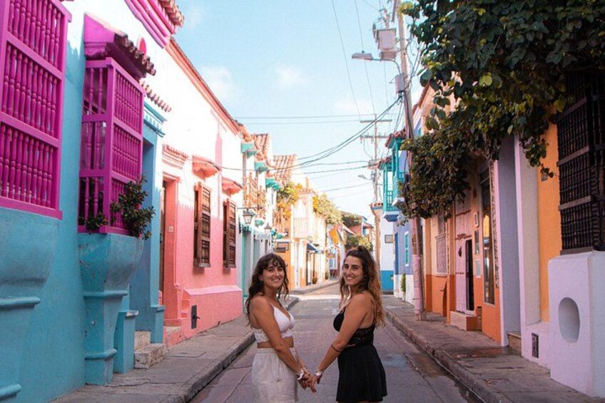 A narrow street with colorful buildings, a woman in a white dress, and another woman in a black dress holding hands. 5