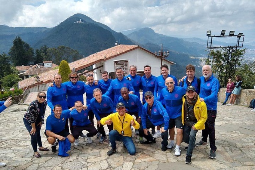 A group of people in blue jackets posing on a stone-paved area with a mountain and buildings in the background. 4