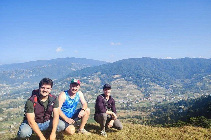 Drie personen zitten op een grasheuvel, met een bergachtig landschap op de achtergrond. 1