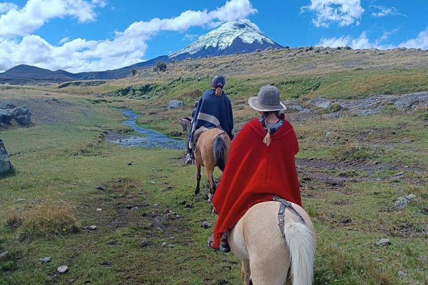 Twee personen rijden te paard op een begroeiing pad, met een berg op de achtergrond. 1