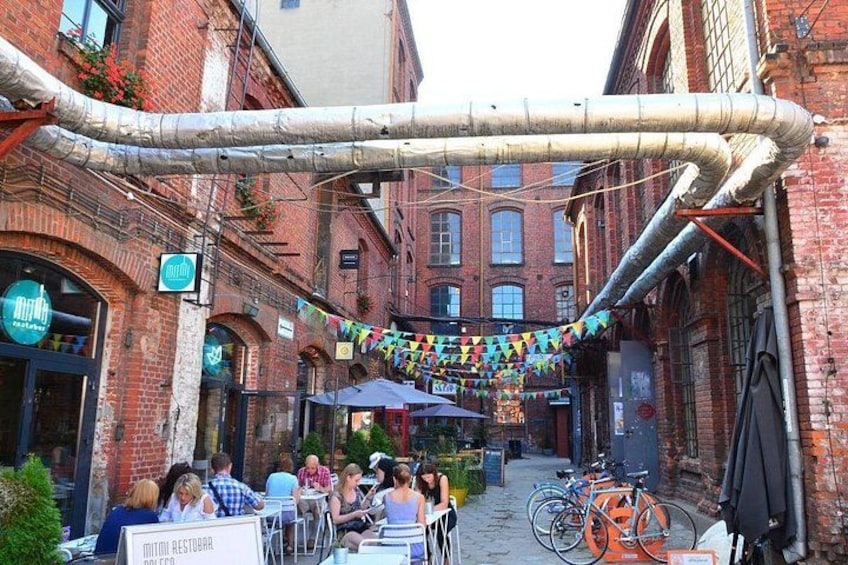 A narrow alley with brick buildings, outdoor seating, and bicycles. 2