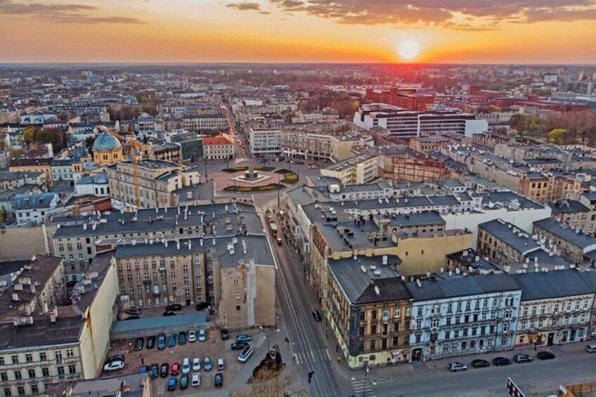 A cityscape at sunset with a prominent building with a dome, a wide street, and various other buildings. 3