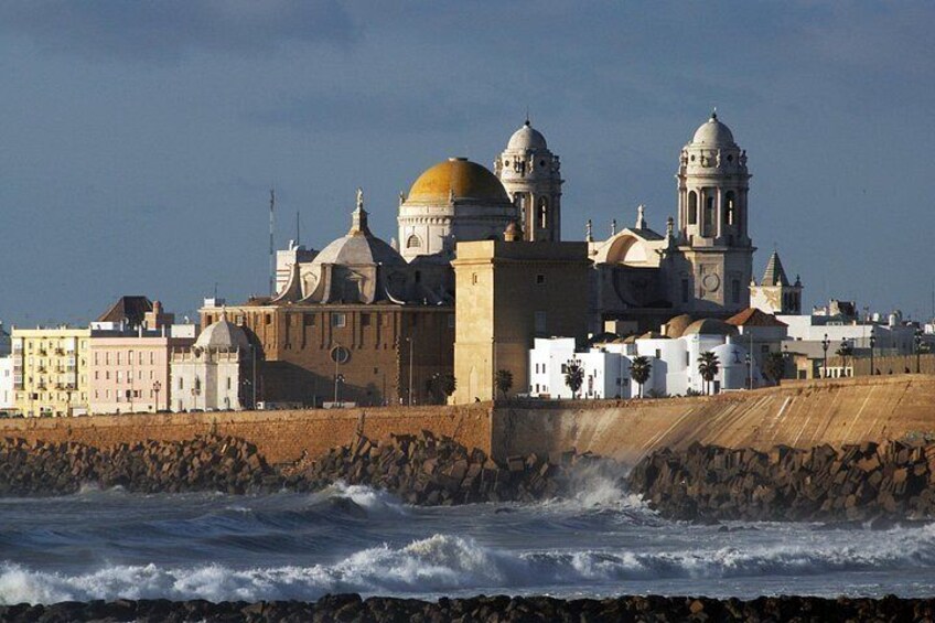 Un paisaje urbano costero con edificios históricos, una costa rocosa y olas rompiendo contra el muro de contención. 1