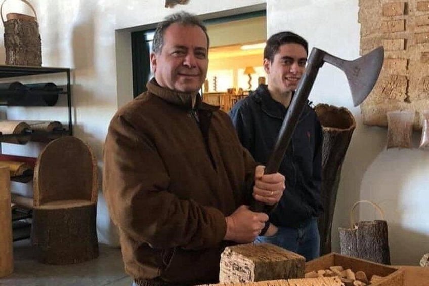 Two people holding an axe and a wooden log in a rustic setting with stone walls and wooden furniture. 2