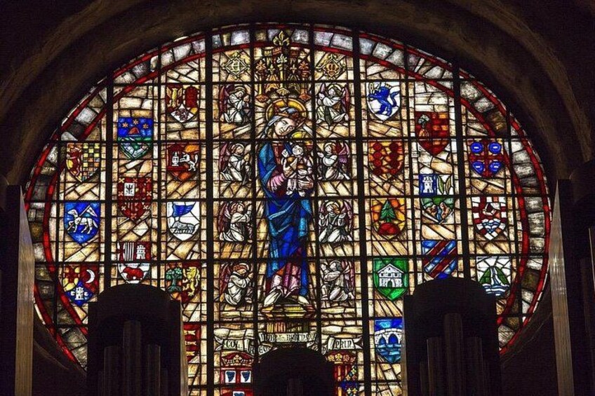 A stained glass window with a central figure, surrounded by various colored panels and designs. 1