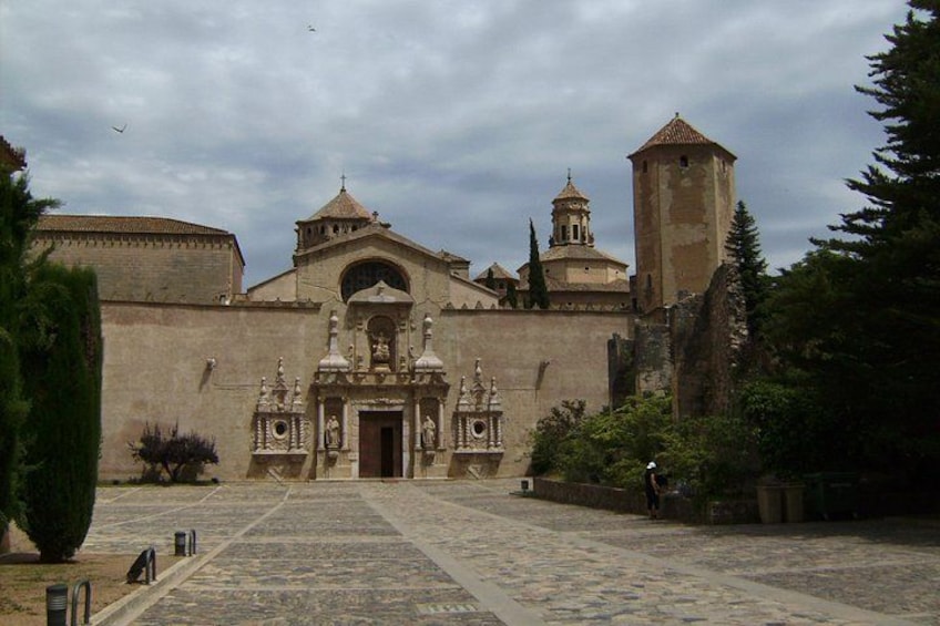 Un edificio histórico con una entrada central, una torre de campanas y un patio con pavimento decorativo. 4