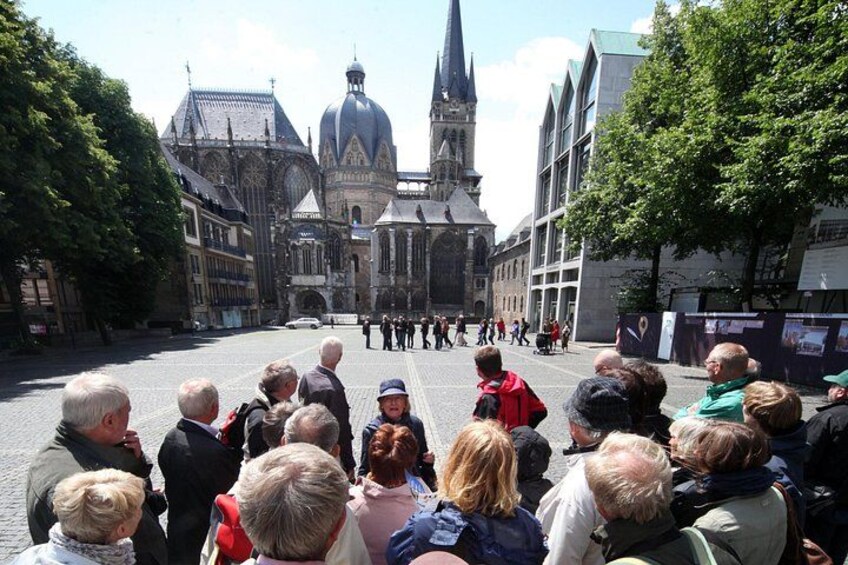 A group of people gathered in a square with historic buildings in the background. 1