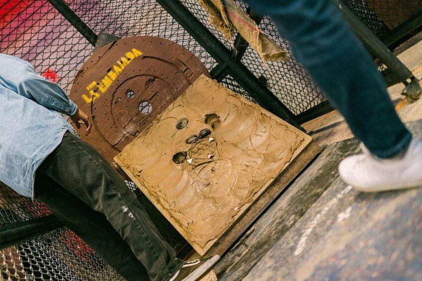 Een persoon staat op een houten platform met een metalen hek, een kartonnen doos en een bruin voorwerp met gaten. 3