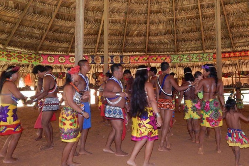 Een groep mensen in traditionele kledij danst in een gebouw met rieten dak. 1