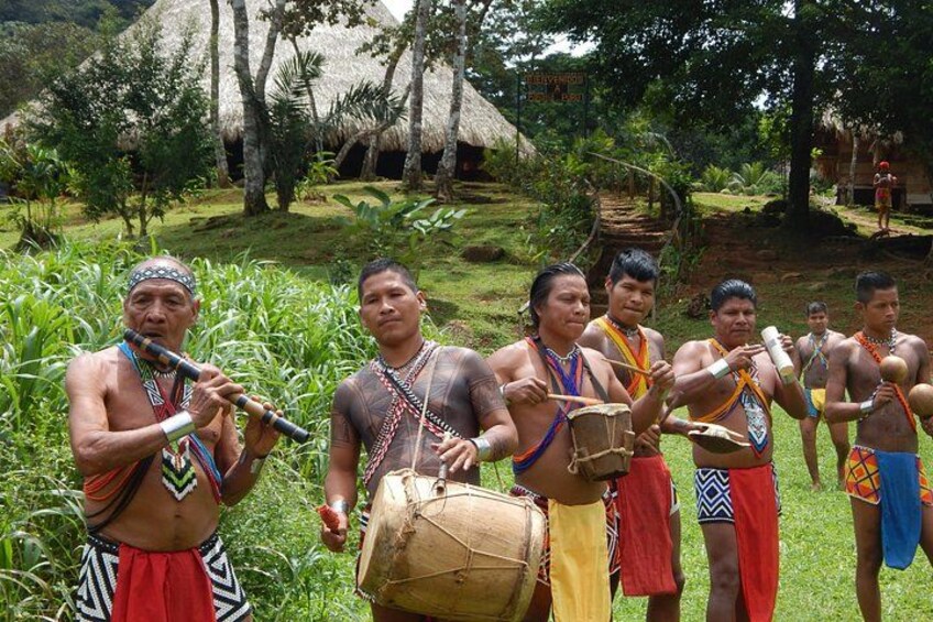 Een groep mensen in traditionele kledij die drums bespelen in een weelderige, groene omgeving. 4