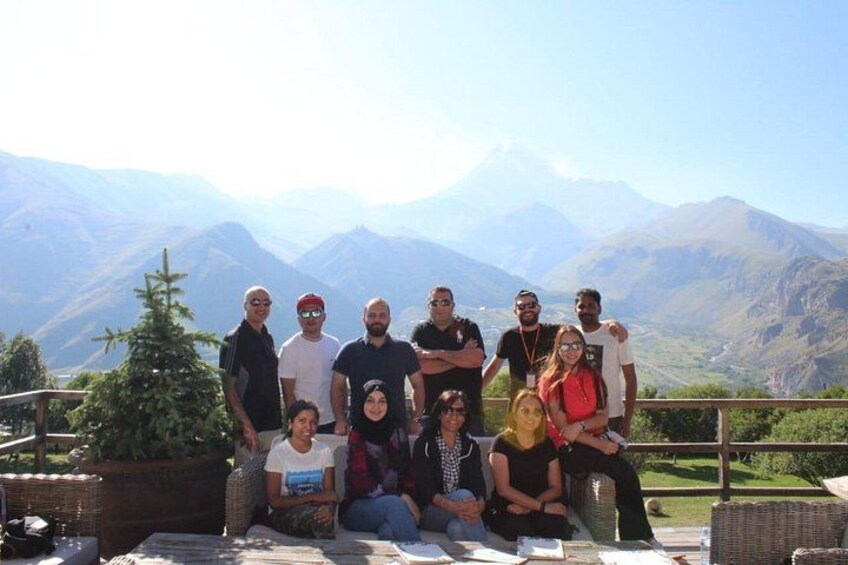 A group of people posing on a terrace with a mountainous landscape in the background. 1