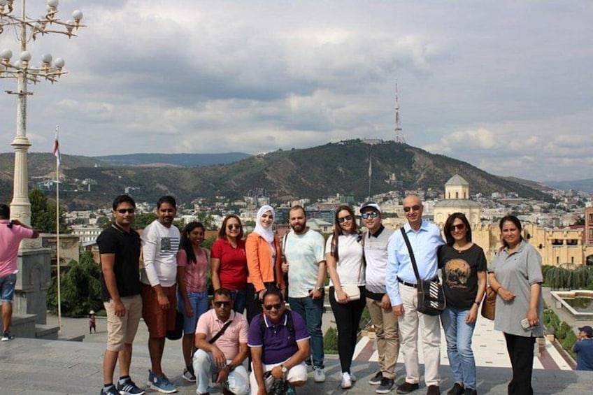 A group of people standing on a terrace with a cityscape and a hill in the background. 3