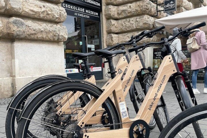 A wooden bike rack with a sign, a stone building, and a person walking in the background. 4