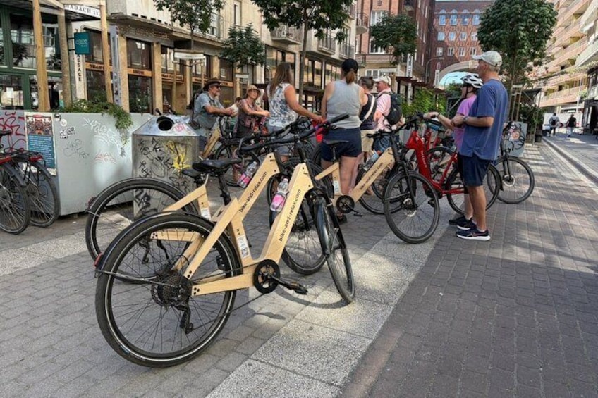 A group of people standing near bicycles parked on a sidewalk in an urban setting. 5