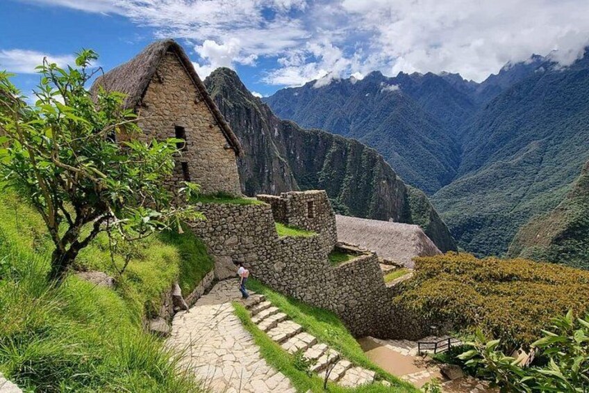 A stone building with a thatched roof, surrounded by lush greenery and steep mountains in the background. 5