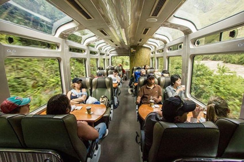 A train interior with passengers seated at tables, windows showing greenery outside. 5