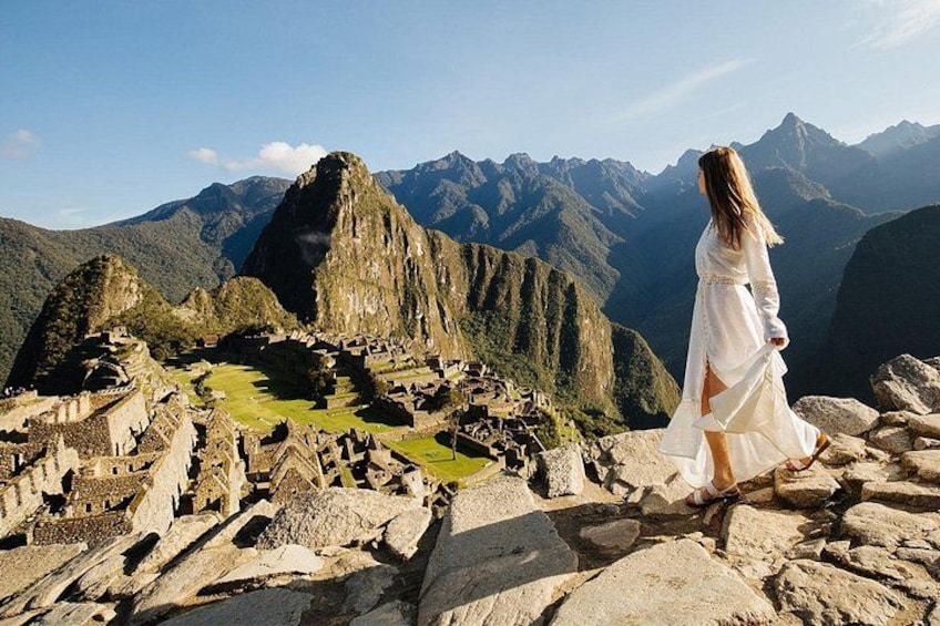 A person in a white dress standing on ruins with mountains in the background. 1