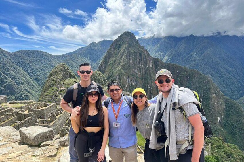 En gruppe mennesker ved Machu Picchu med antikke ruiner og et bjergrigt landskab i baggrunden. 2