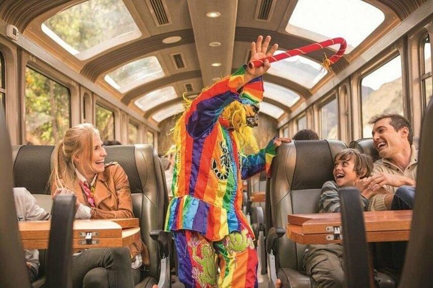 A train interior with passengers seated, a clown performing, and a window showing a mountainous landscape. 4