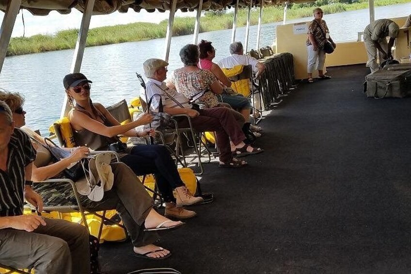 Mensen zitten op een boot, sommigen met bagage, aan een rustig water. 2
