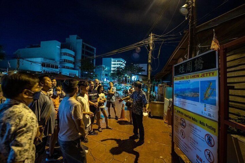 A nighttime street scene with a crowd of people gathered around a food stall. 2