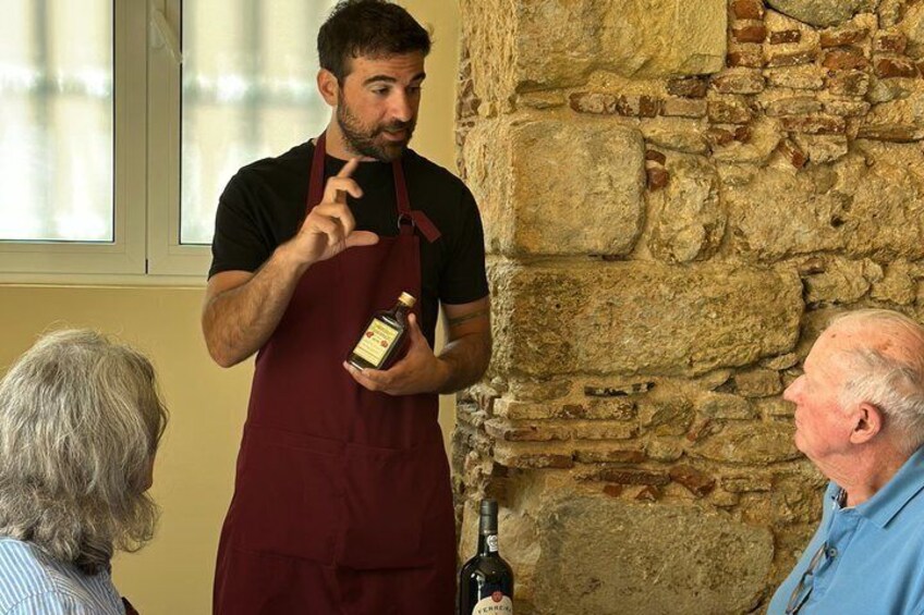 A person in a red apron holding a bottle, standing in front of a stone wall. 4