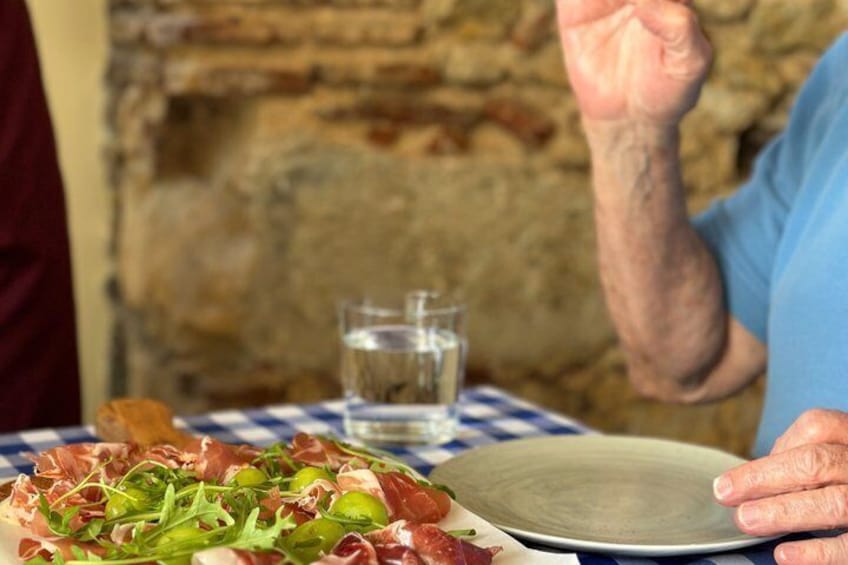 A person holding a plate with a salad and a glass of water on a checkered tablecloth. 5