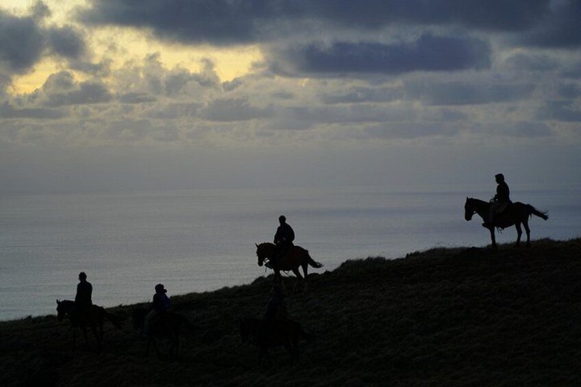 Silhouettes of people riding horses on a hill with a body of water in the background. 4