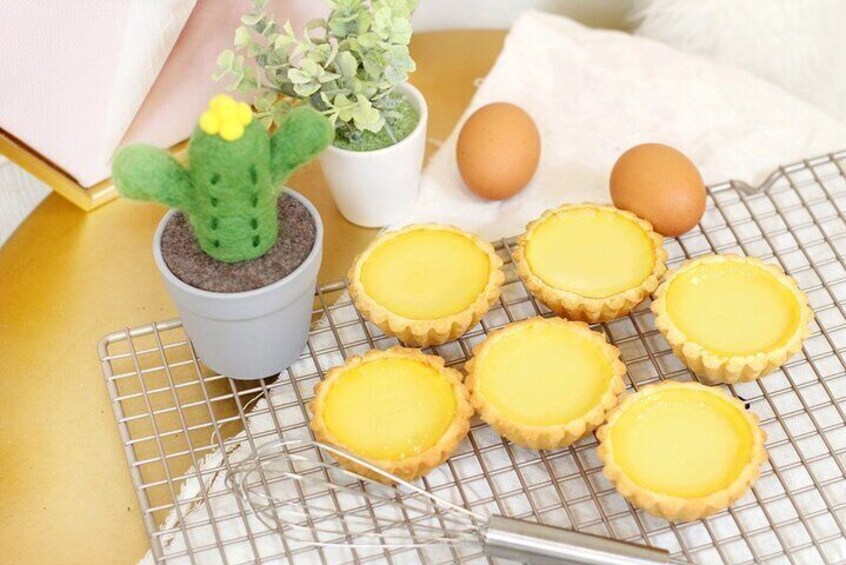 Six tartelettes à la crème jaune sur une grille métallique, un petit cactus en pot et deux œufs bruns posés sur un tissu blanc. 4