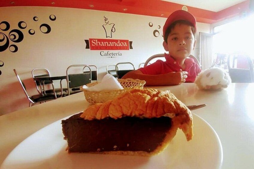A dessert with a chocolate base and a crispy topping, a white plate, and a table with a logo for 'Shanandoak Calería' in the background. 4