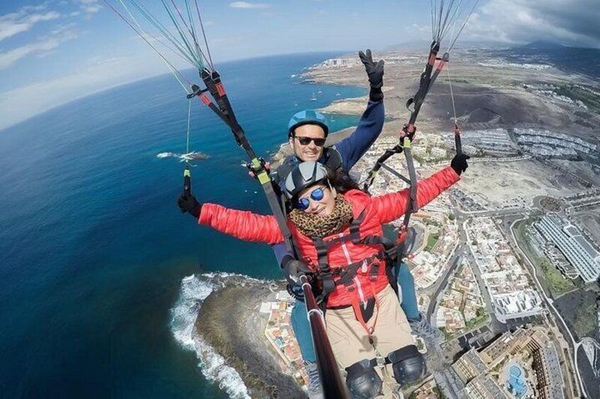 Una persona practicando parapente sobre una zona costera con edificios y el océano abajo. 1