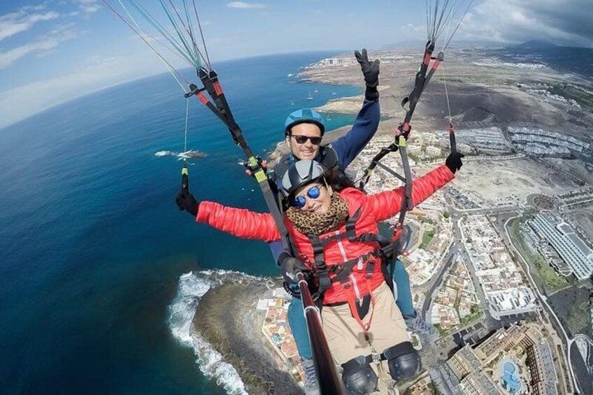 A person paragliding over a coastal area with buildings and the ocean below. 1