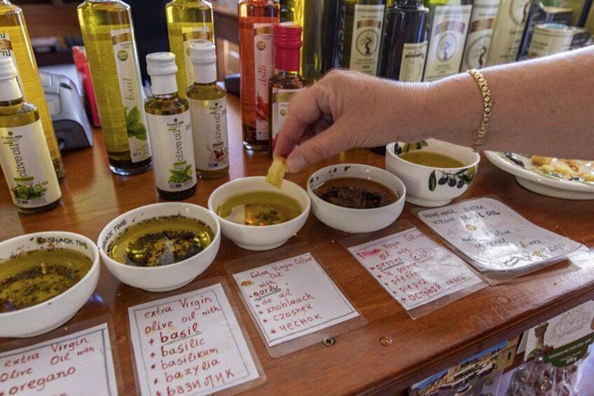 A person dipping a piece of food into a bowl of olive oil-based sauce, with various bottles of sauces and condiments in the background. 4
